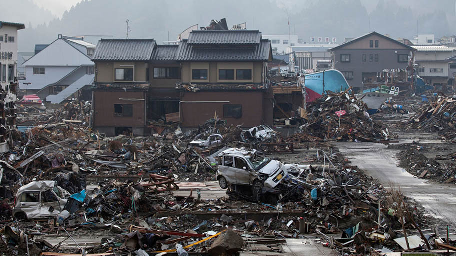 City block with broken cars and houses surrounded by debris from tsunami