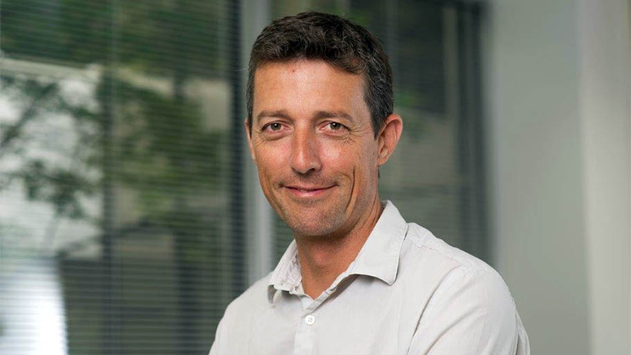 Head and shoulders shot of man in white shirt in front of window