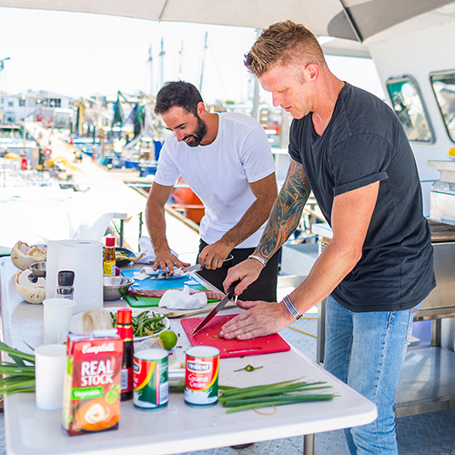 Table of ingredients (centre left) with chefs chopping food (right)