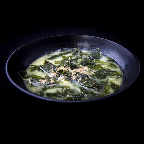Seaweed soup in dark bowl, with spice garnish