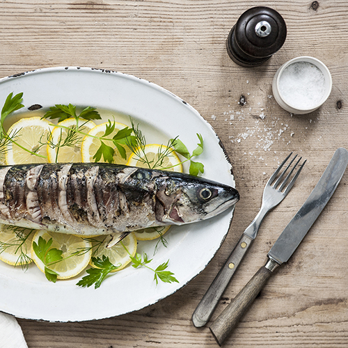 Mackerel dish (left) on a wooden table with utensils and salt and pepper (right)