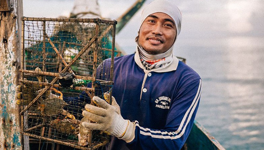 Fisherman in blue tracksuit top holding bamboo trap with crabs inside
