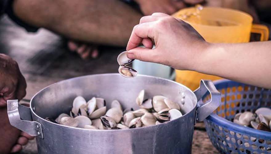 Hand placing clams in metal pot