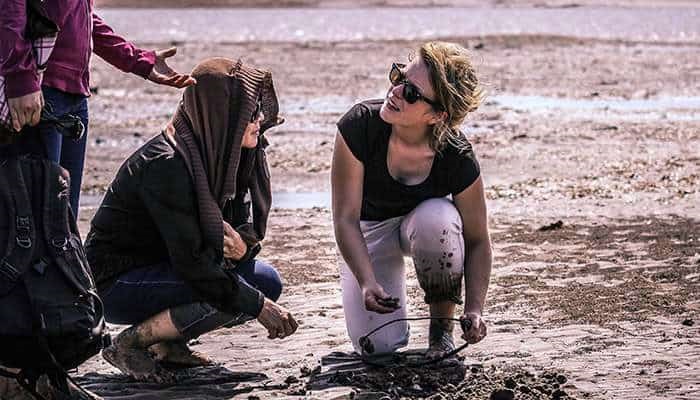 Women in sunglasses crouching on muddy sand by clam harvest