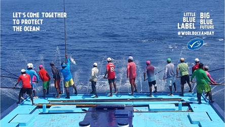 Pole and line fishers standing and casting lines off back of boat, with MSC logo and World Ocean Day message