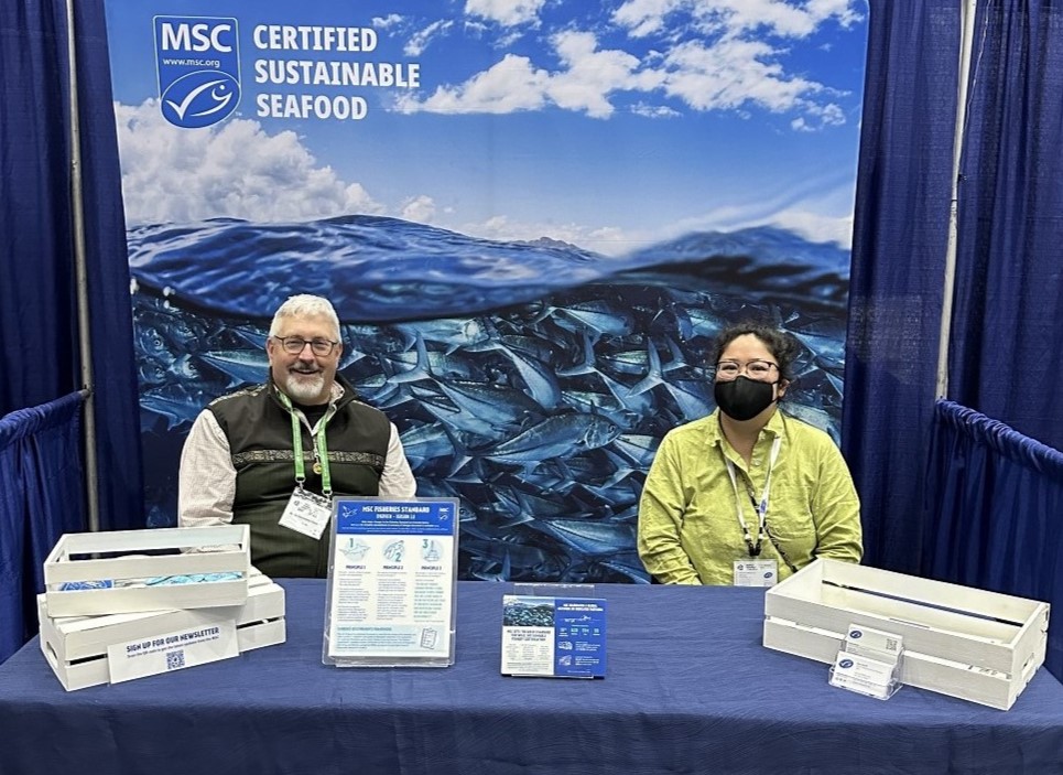Two MSC staff sitting behind a booth with a blue tablecloth and ocean background