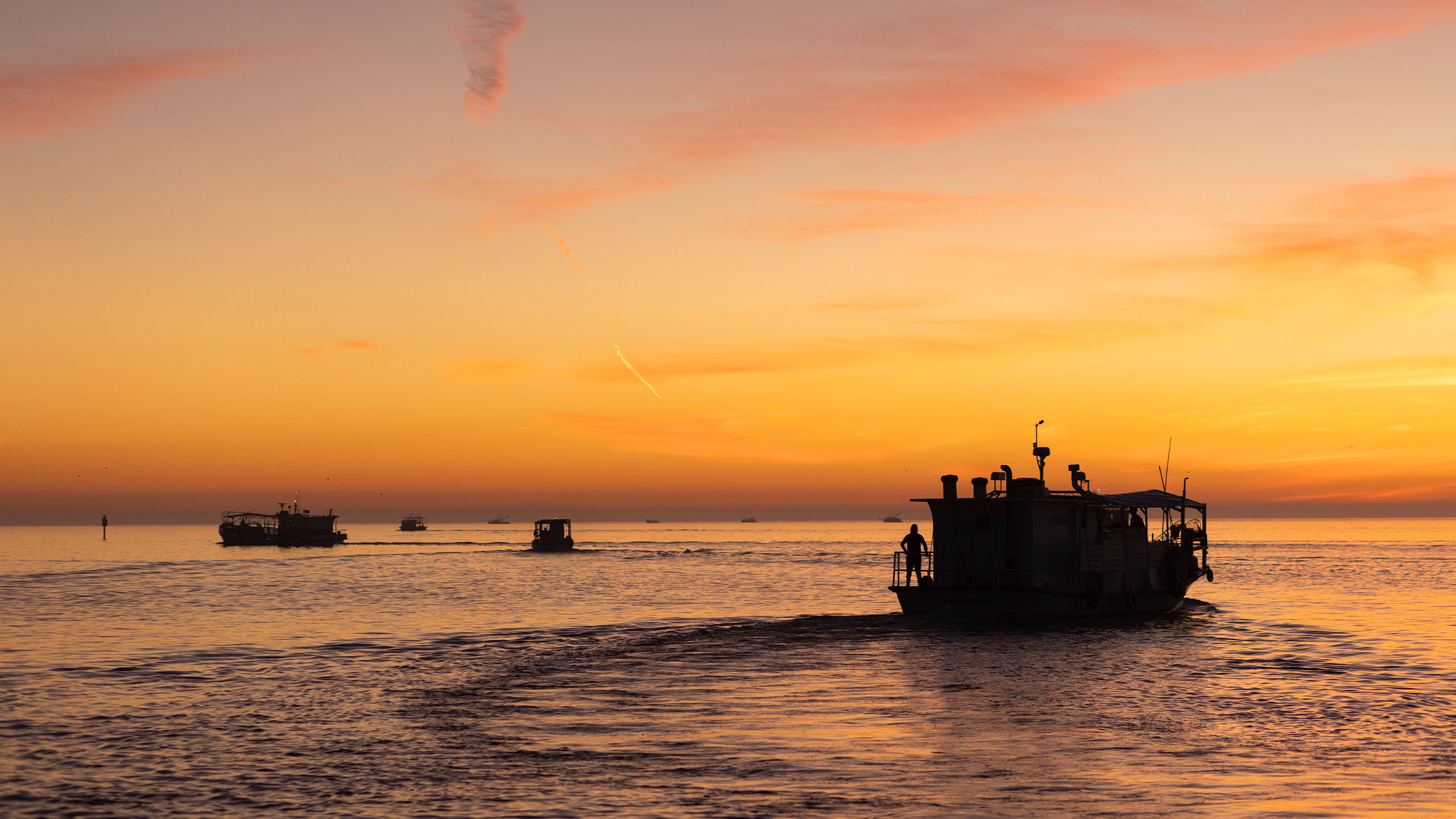 A medium sized boat heading out to sea at sunset