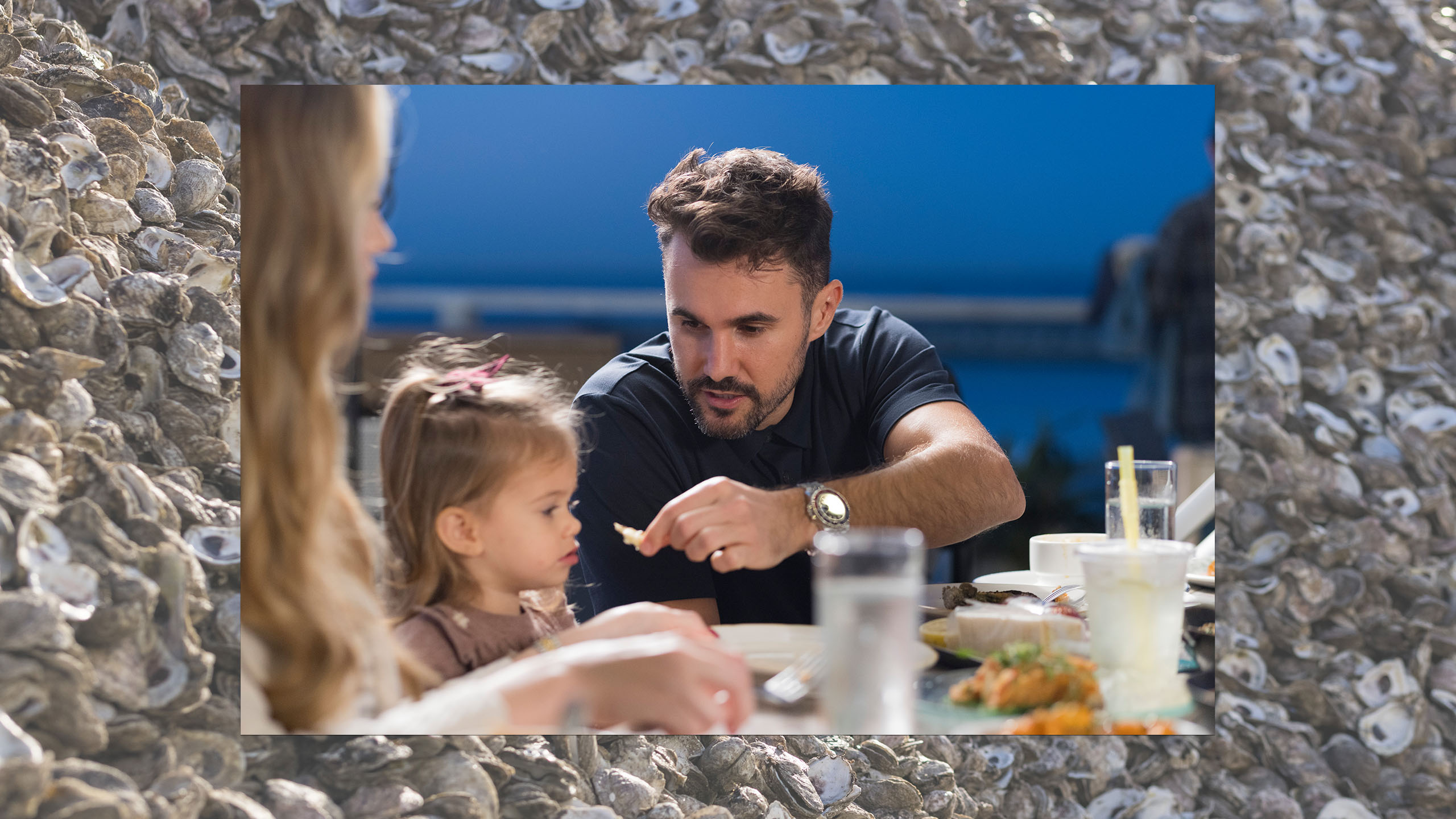 Man offering an oyster to his young daughter
