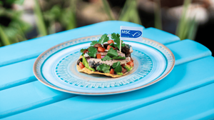 A sardine tostada on a white plate over a blue table