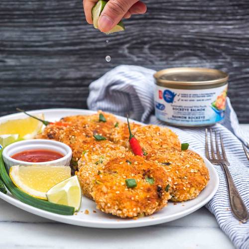 Five salmon cakes on a white plate with red dipping sauce