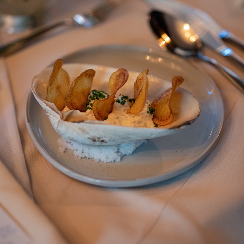 A clam shell holding clam dip with five potato chips sticking up from it