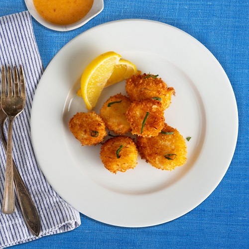 Fried scallops on a white plate with lemon on a blue table cloth