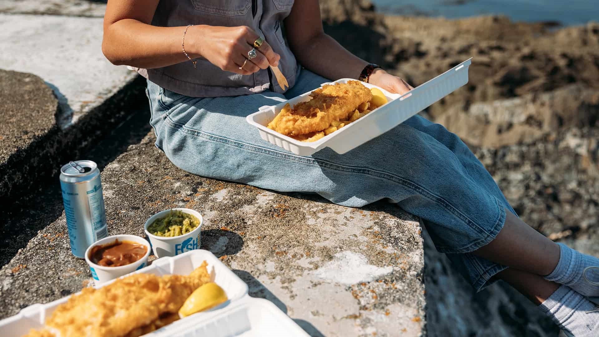 Fish and chips being eaten out of a box next to the sea