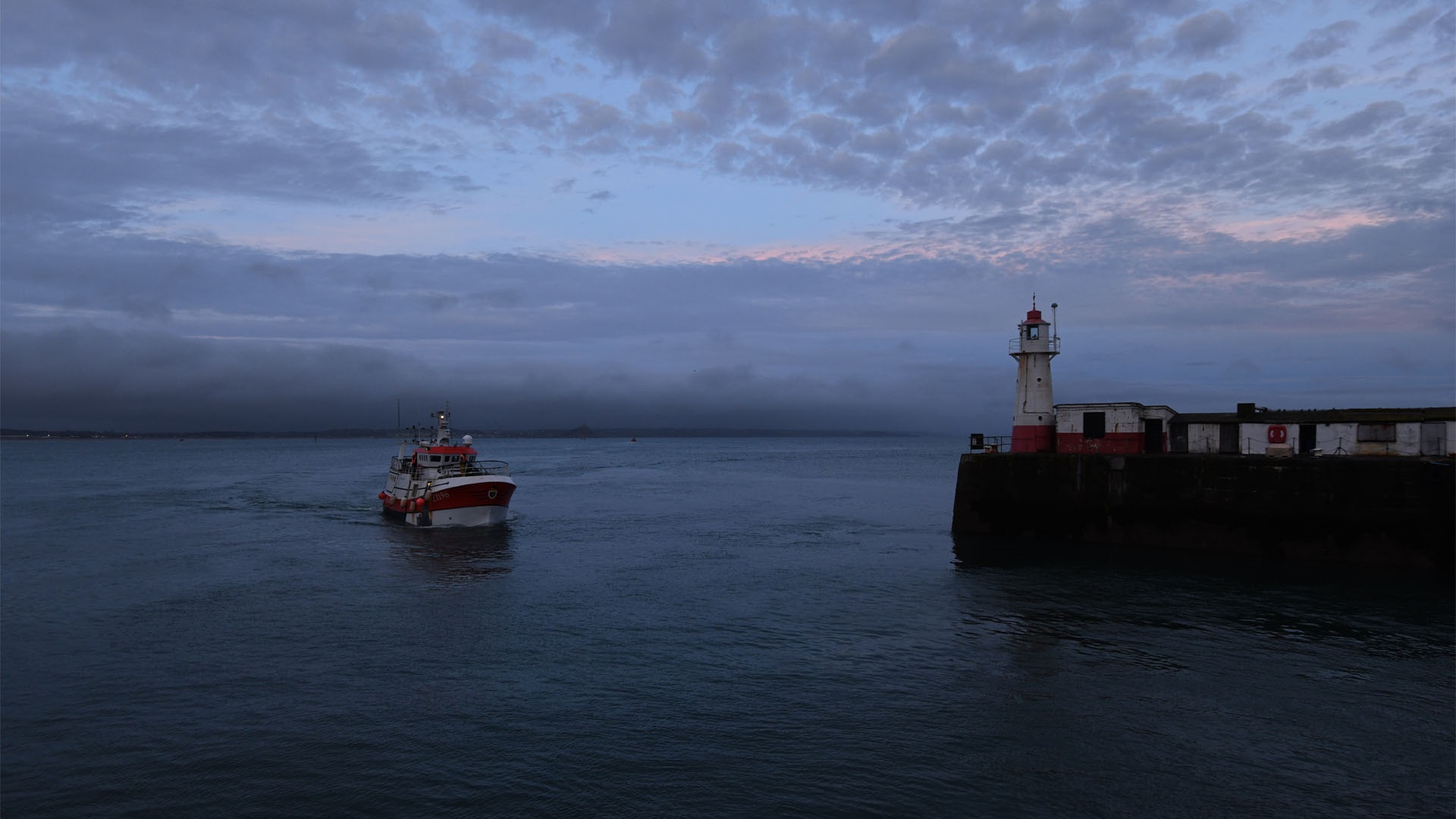 Hake fishing boat sailing next to lighthouse