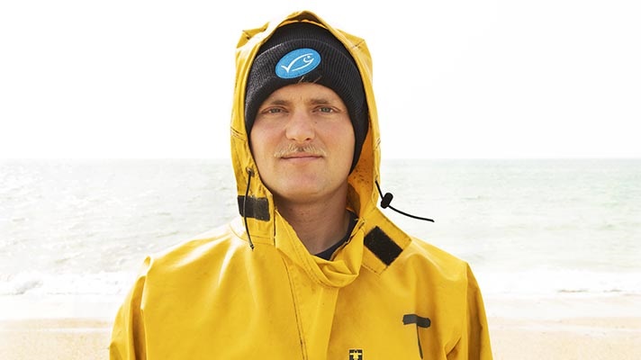 Headshot of fisherman in yellow jacket and woolen hat